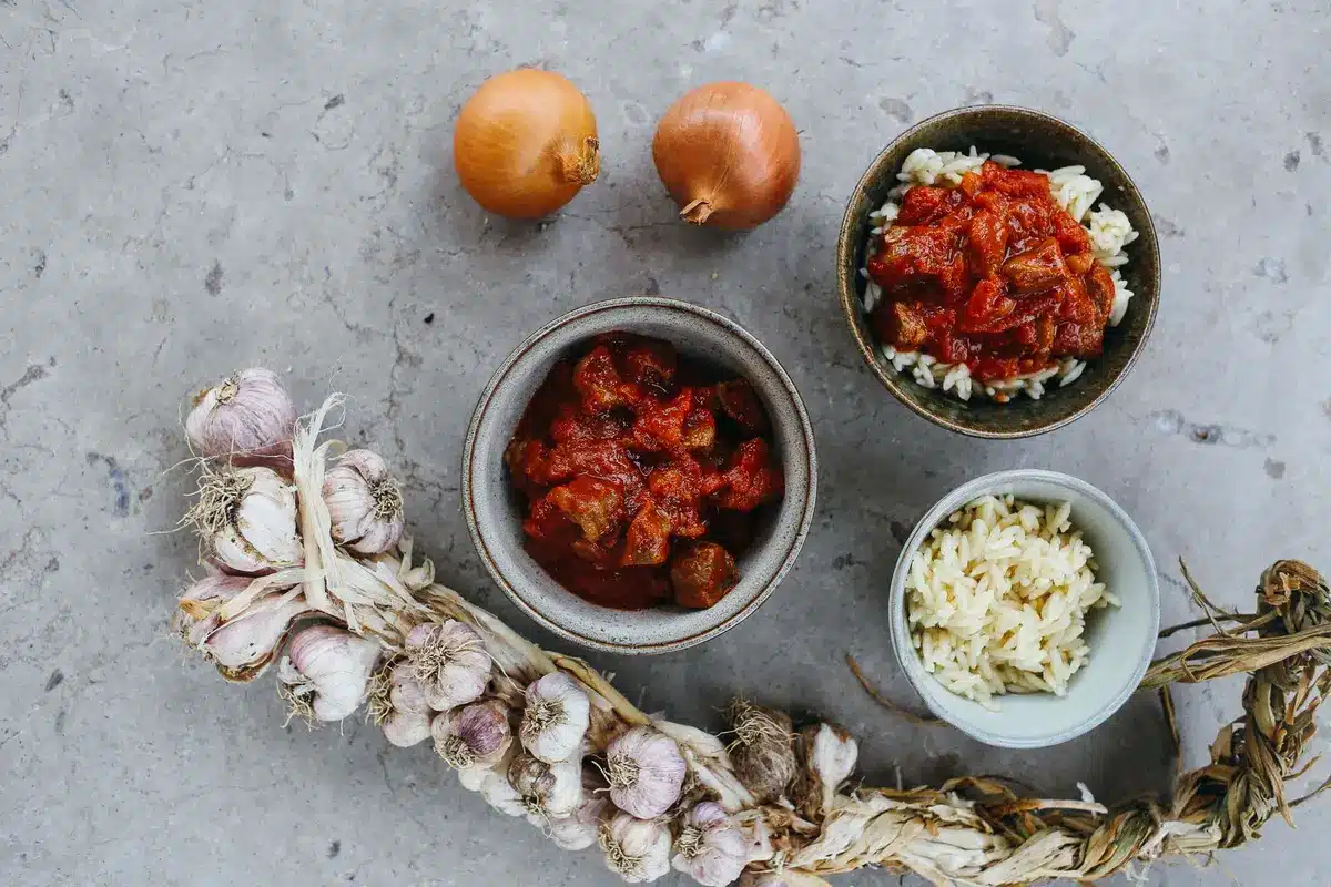 Ingrédients du rougail saucisse : saucisses fumées, tomates concassées, oignons émincés, ail et épices sur une surface d