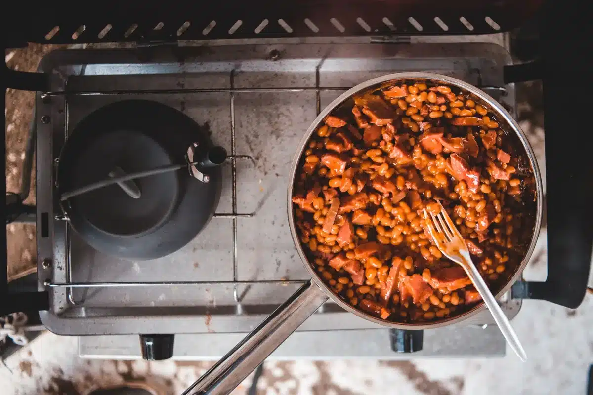 Casserole contenant des rondelles de saucisse fumée, tomates et oignons en train de mijoter à feu doux
