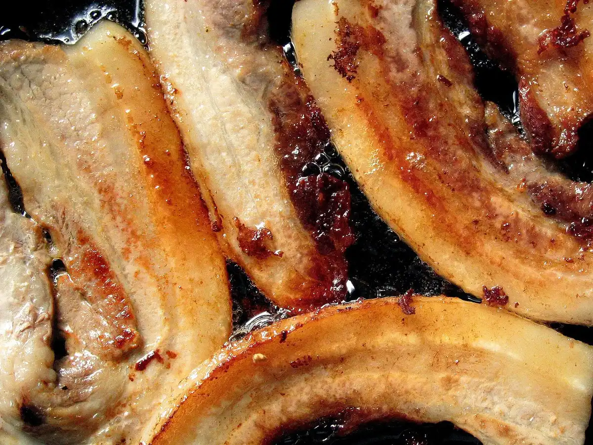 Bacon en train de cuire dans une poêle jusqu'à devenir croustillant