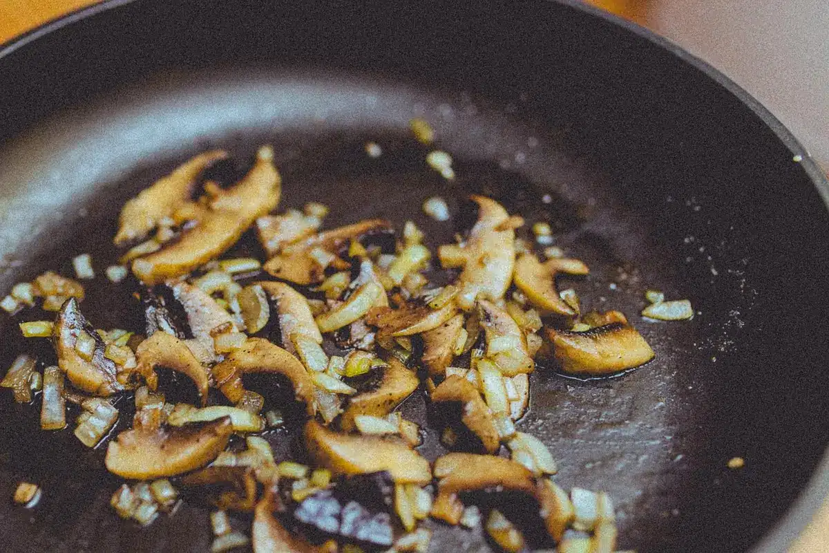 Poêle avec oignon translucide et champignons dorés en train de cuire