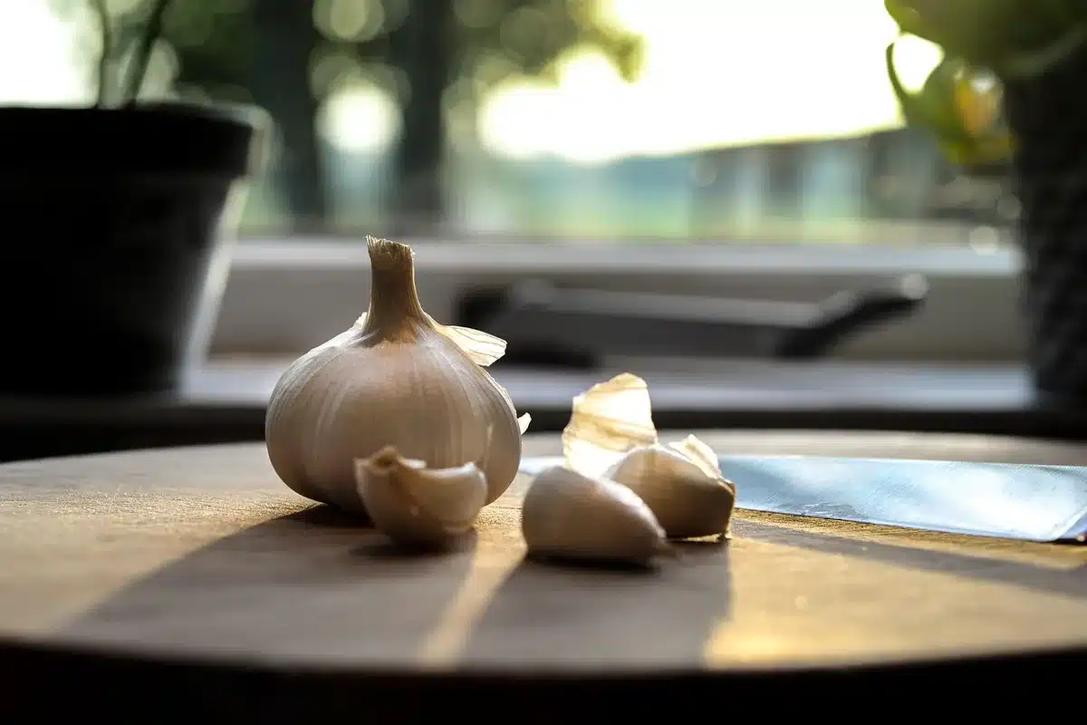 Pâte à flammekueche étalée sur une plaque avec ingrédients et mains préparant la tarte